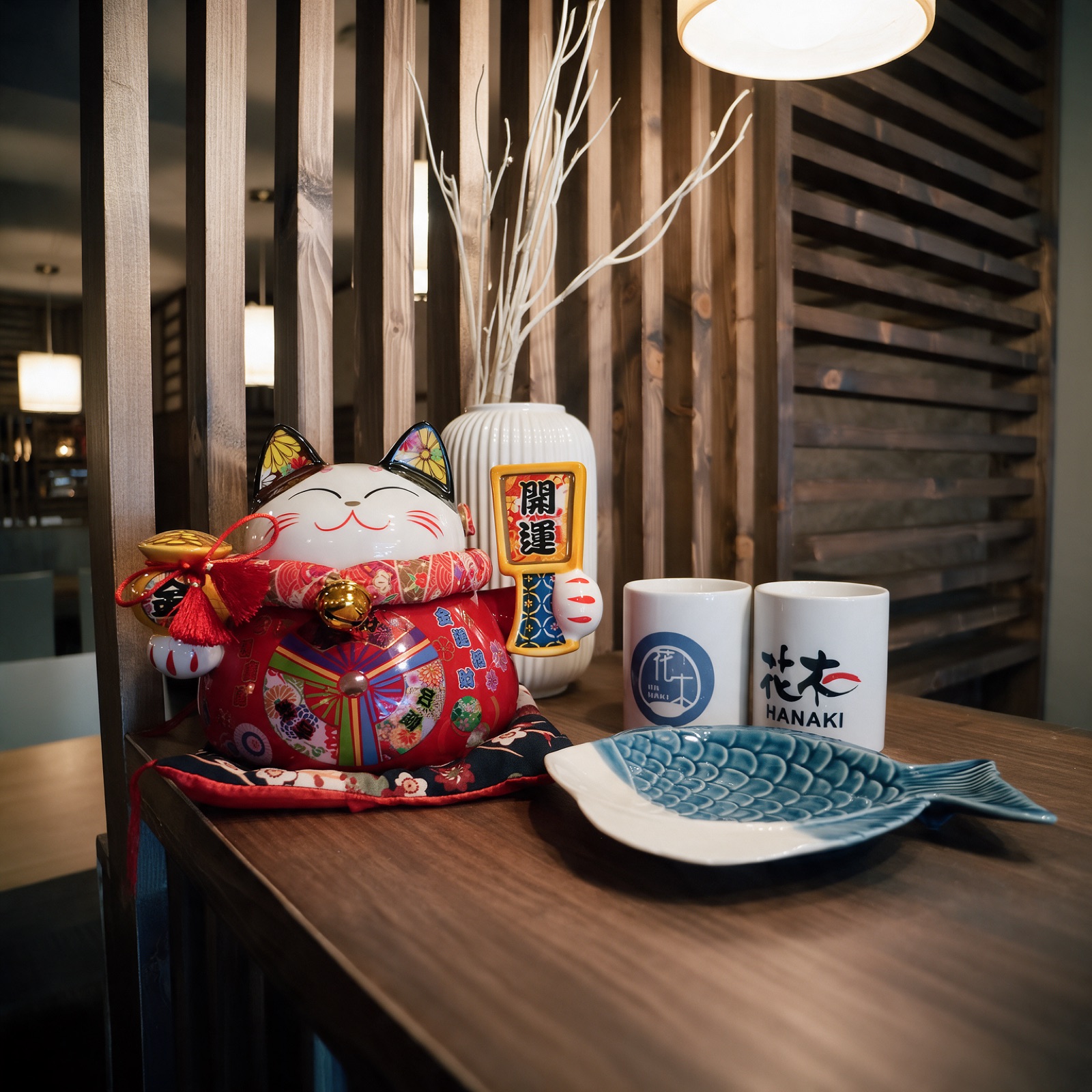 Maneki-neko y vasos de té Hanaki junto a la celosía de madera